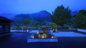 A serene outdoor area with a stone fountain, a traditional building, and a mountainous backdrop. - Imurakebettei Tsukinohanare (Asakura)