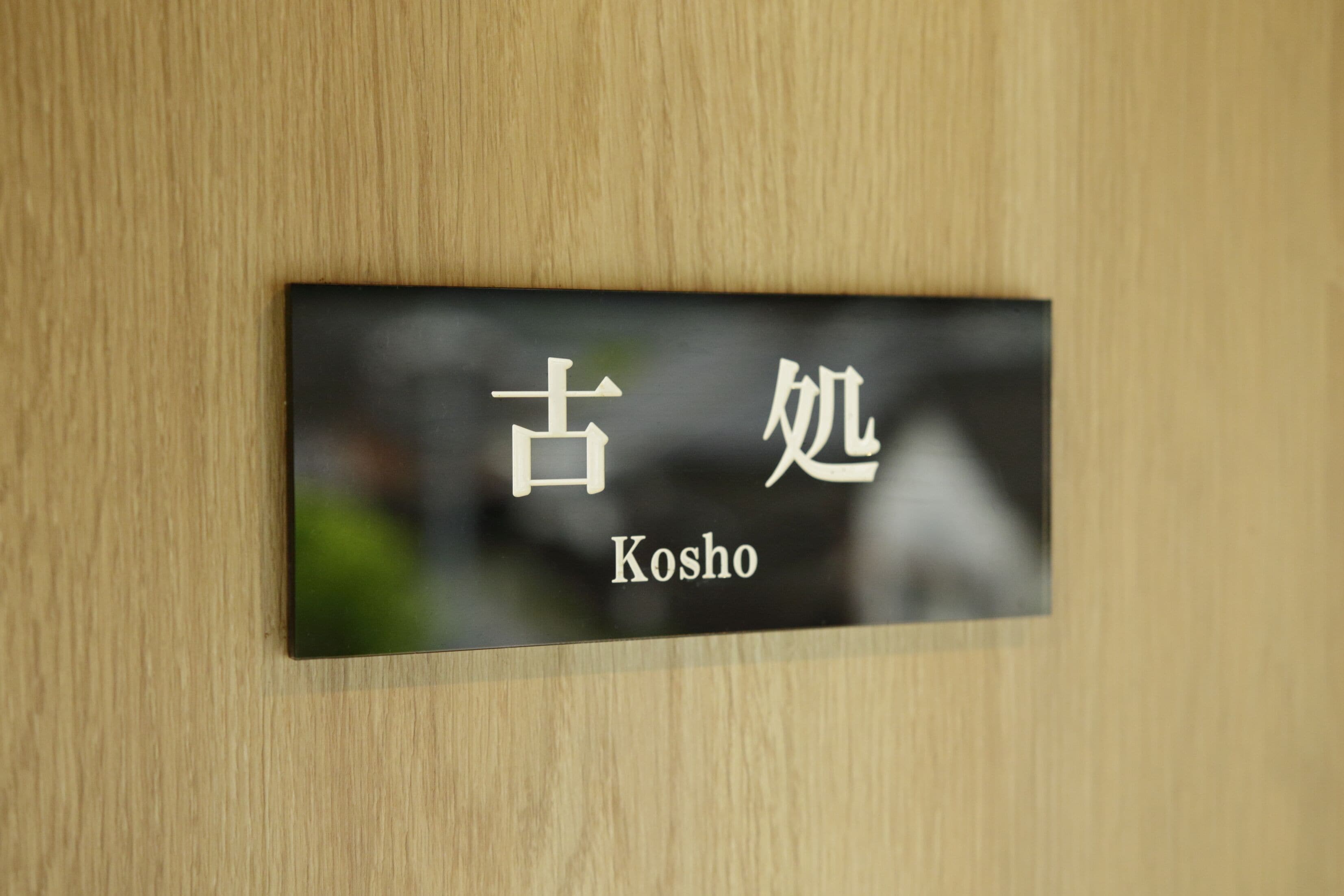 A sign with Japanese characters and the English word "Kosho" on a wooden wall.