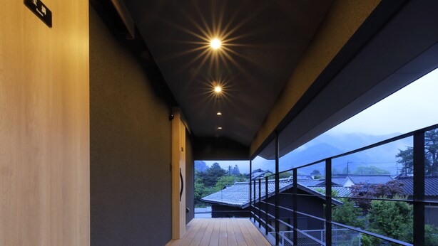 A corridor with wooden flooring, a balcony with a railing, and a view of buildings and greenery. - Imurakebettei Tsukinohanare (Asakura)