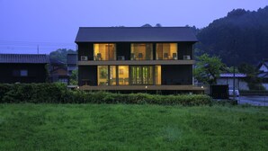 A modern two-story house with large windows and a flat roof, surrounded by greenery and hills. - Imurakebettei Tsukinohanare (Asakura)