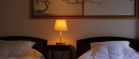 A hotel room with two single beds, a bedside table with a lamp, and artwork on the wall.
