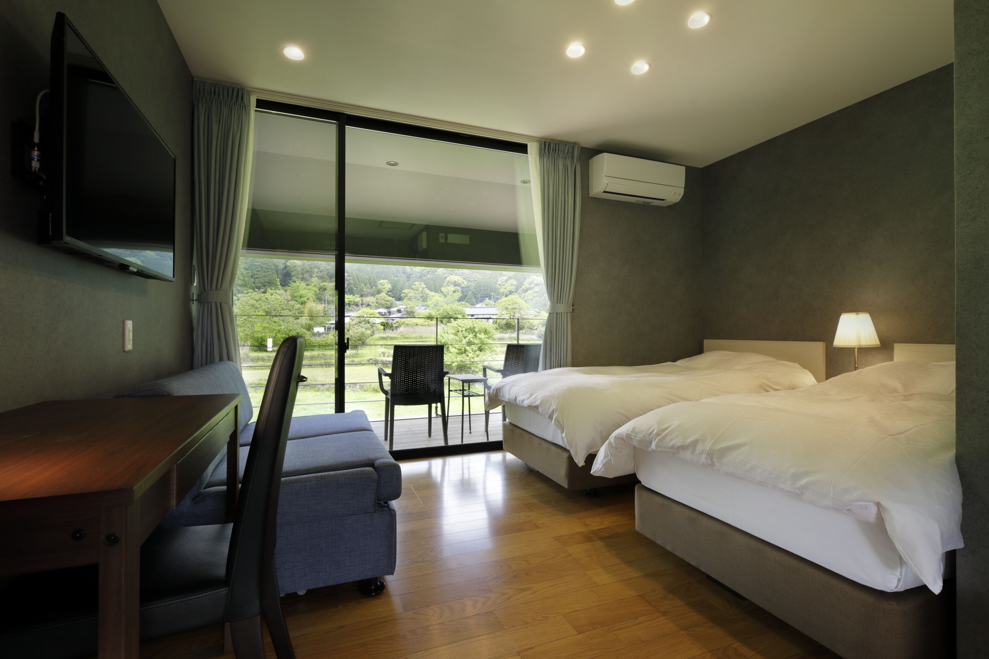 Quarto de hotel com escrivaninha, duas camas, televisão e vista para área verde.