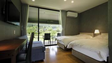 Quarto de hotel com escrivaninha, duas camas, televisão e vista para área verde.