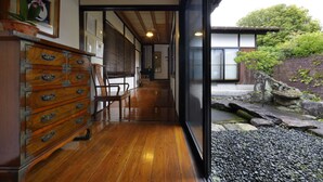 A traditional Japanese interior with wooden flooring, a sliding door leading to a garden, and a wooden dresser with multiple drawers. - Imurakebettei Tsukinohanare (Asakura)