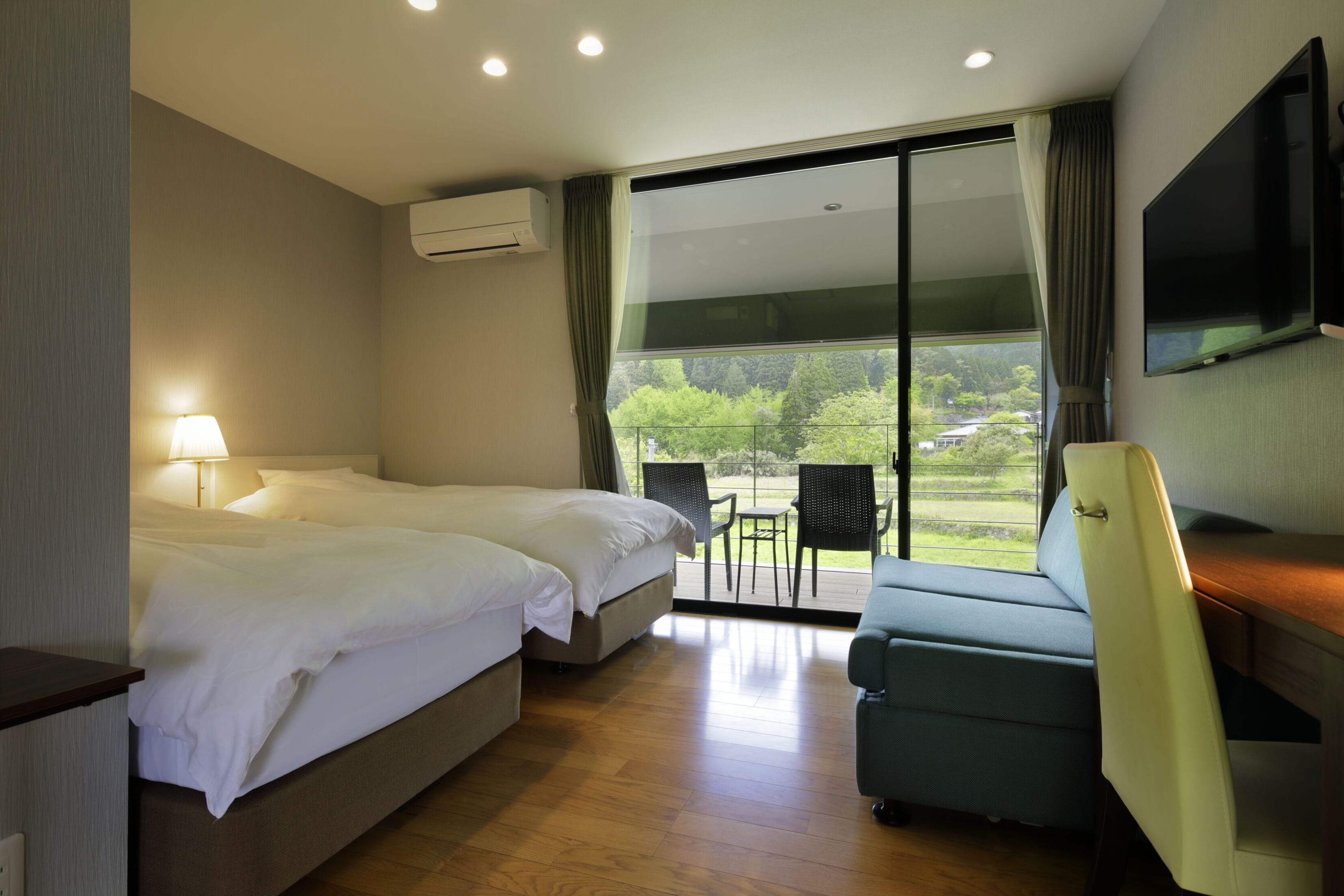 A hotel room with two beds, a TV, a desk, and a balcony with chairs.