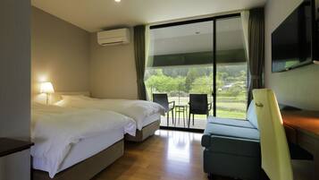 A hotel room with two beds, a TV, a desk, and a balcony with chairs.