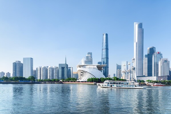 A city skyline with modern skyscrapers and a distinctive white building with a curved roof by the water. - Hi Inn Liangpin Guangzhou Shaheding Metro Station (Guangzhou)
