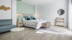 Une chambre moderne avec un lit, un canapé bleu, une table basse ronde, une commode et un luminaire suspendu.