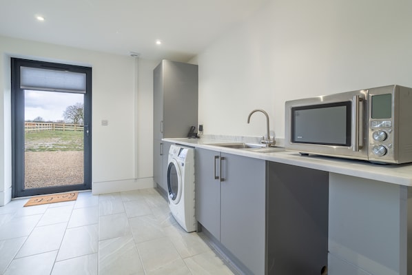 A compact kitchen with a washing machine, a microwave, and a sink. - Mandalore, Henham, Suffolk (Henham)
