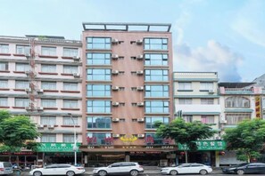 Een hotel met meerdere verdiepingen, een centrale ingang, diverse balkons en borden met namen van verschillende bedrijven.