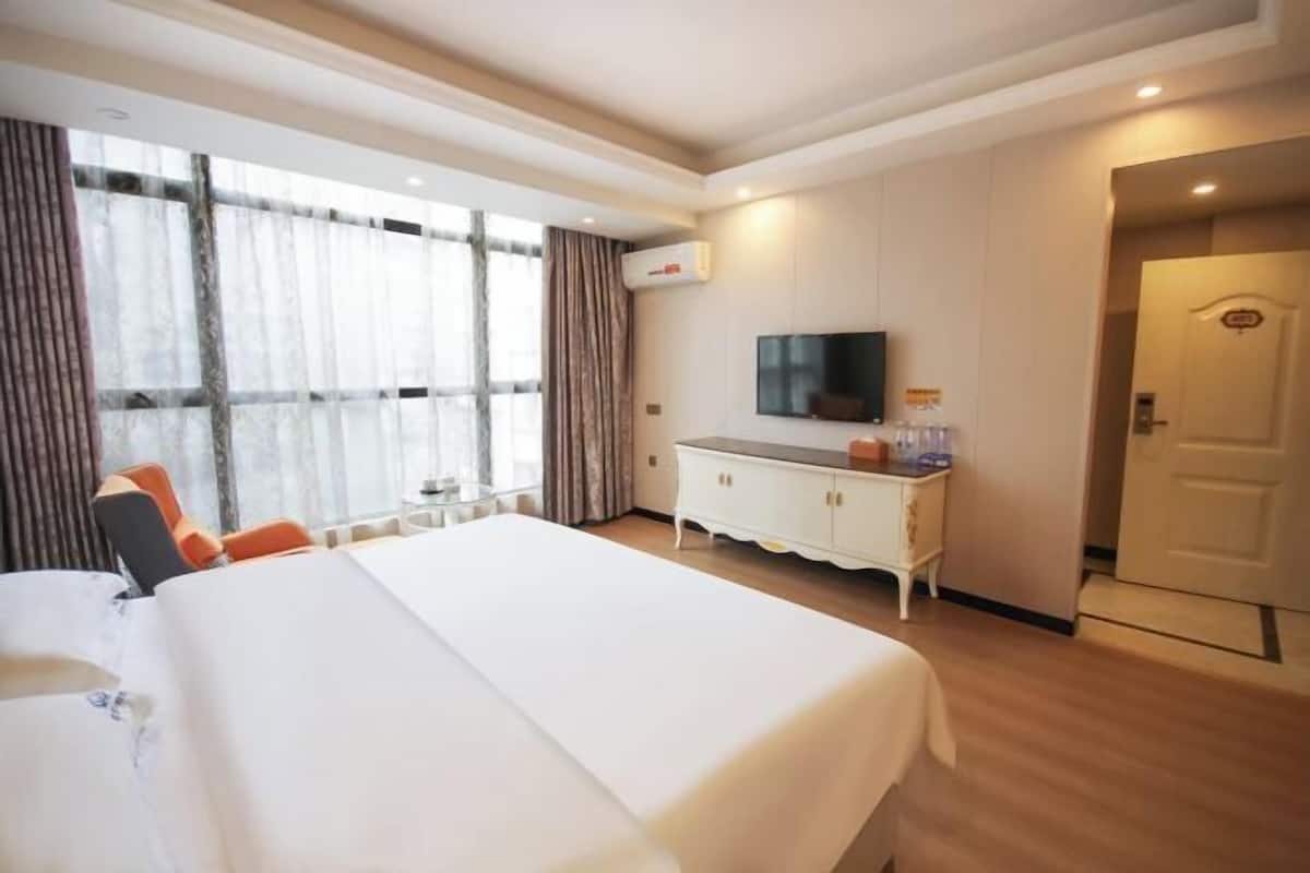 Ein Hotelzimmer mit einem großen Bett, einem Fernseher auf einem weißen Schrank und einer Tür rechts.