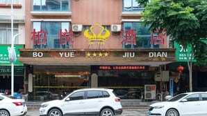 Un hotel con un letrero llamativo que muestra el nombre 'BO YUE DIAN' y un logotipo de corona. Hay dos coches blancos estacionados adelante.