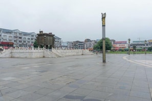 A public square with a central monument, paved with large stone tiles, surrounded by a low stone wall and a staircase leading up to a building.