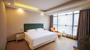Habitación de hotel con una cama grande, una mesita pequeña, una silla y un ventanal con cortinas.