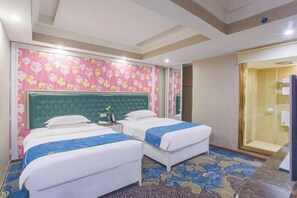 Habitación de hotel con dos camas, alfombra estampada, cabecero verde y ducha con cerramiento de vidrio.