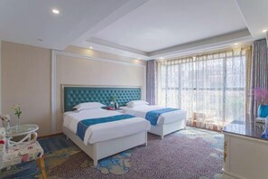 Habitación de hotel con dos camas, un ventanal con cortinas, una mesa redonda con un florero y una alfombra estampada.