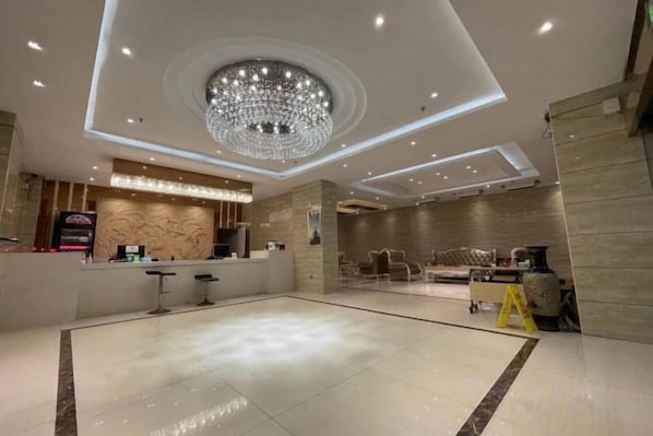 A hotel lobby with a reception desk, a chandelier, and a seating area.