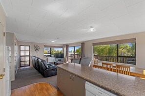 A modern kitchen with a built-in dishwasher, a dining area with wooden chairs, and a large window offering a view of trees.