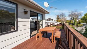 Eine Holzterrasse mit Tisch und Stühlen, einer Satellitenschüssel und Blick auf die Nachbarschaft.