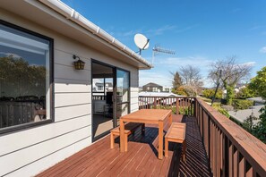 Eine Holzterrasse mit Tisch und Stühlen, einer Satellitenschüssel und Blick auf die Nachbarschaft.