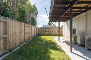 Un patio trasero con cerco de madera, césped y un área de patio cubierta con equipos de aire acondicionado.
