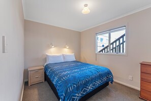 Ein Schlafzimmer mit einem Bett, Nachttischen, einem Fenster mit Aussicht und einer Deckenleuchte.