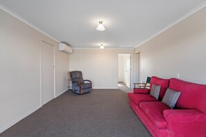 Ein geräumiges Wohnzimmer mit einem roten Sofa, einem grauen Sessel und einer Deckenleuchte.
