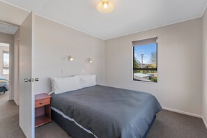 A bedroom with a bed, a nightstand, a window with a view, and a door.