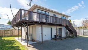 Ein zweistöckiges Haus mit einer überdachten Terrasse, einer Garage und einem eingezäunten Hinterhof.