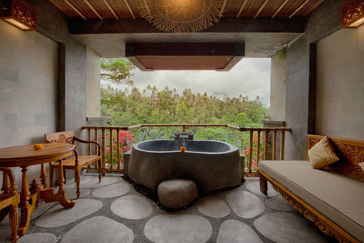 A room with a stone floor, a wooden bench, a table, a sofa, and a large stone bathtub.