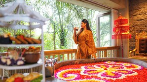 A woman standing by a window overlooking a garden, with a decorative flower arrangement and a buffet table visible. - Kastara Resort (Ubud)