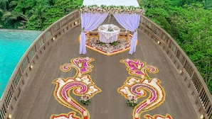A wooden deck with a central table and chairs, surrounded by floral decorations and a view of a lush green forest. - Kastara Resort (Ubud)