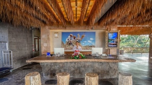A reception desk with a thatched roof, a painting of a tropical scene, and a monitor on the wall. - Kastara Resort (Ubud)