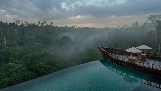 An infinity pool with a view of a lush forest and a boat with umbrellas. - Kastara Resort (Ubud)
