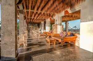 A spacious indoor area with a thatched roof, wooden furniture, and a view of the sea.