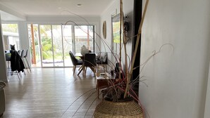 A spacious hallway with a large woven basket on the floor, a dining area with chairs and a table, and a view of the outdoors through large windows.