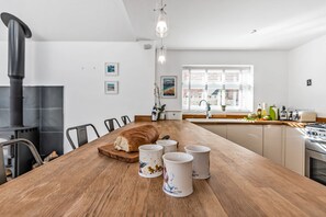Uma cozinha moderna com uma mesa de madeira, quatro canecas de cerâmica, um pão e um fogão preto.