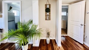 Ein Flur mit Holzboden, einem Blumentopf, einer Vase mit Trockenpflanzen und einem Schild mit der Aufschrift 'HOME'.