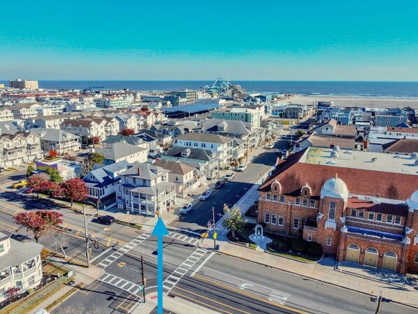 An aerial view of a coastal town with residential buildings, a prominent brick building with a dome, and a clear view of the ocean.