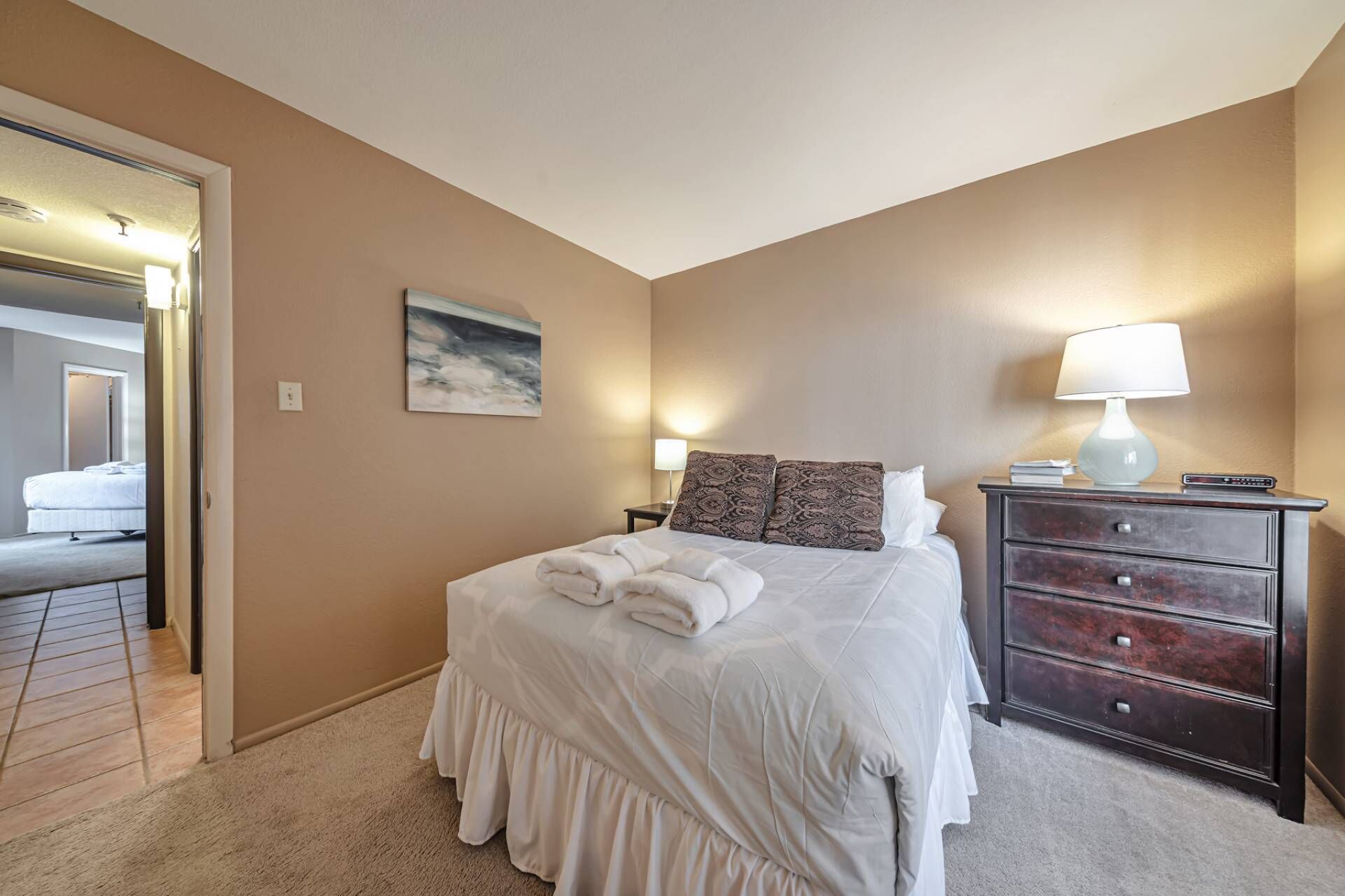 Une chambre d’hôtel avec un lit, une commode, une lampe et un tableau au mur.