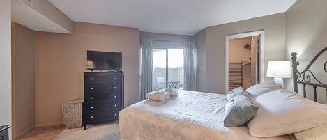 A bedroom with a bed, a dresser, a television, and a window with curtains.