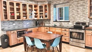 Una cocina moderna con armarios de madera, encimera negra y un comedor con mesa de madera y sillas azules.