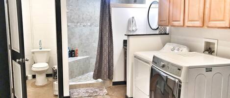 Une petite salle de bain comprenant des toilettes, une douche et un lave-linge.