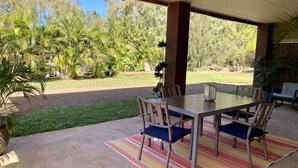 Un patio cubierto con una mesa y sillas, rodeado de follaje y vistas a árboles.