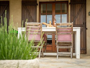 A rustic outdoor seating area with two wooden chairs and a table, set against a building with wooden shutters and a large glass door. - Fine studio with large terrace and views (Cajarc)