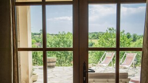 A view through a window with a stone patio, two striped lounge chairs, and a potted plant. - Fine studio with large terrace and views (Cajarc)