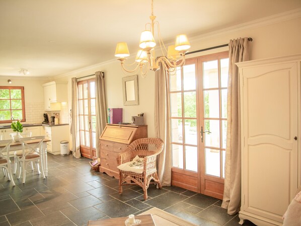 A spacious kitchen with a dining area, large windows, and a wicker chair.