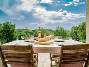 An outdoor dining table with a view of the countryside, a bottle of wine, and a baguette on the table.