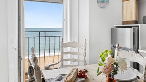 Une pièce donnant sur la côte, avec vue sur la mer, une chaise blanche, une table avec une miche de pain, des tomates et un vase rempli de fleurs.