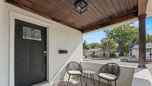 A covered porch with a dark door, two wicker chairs, a small table, and a mailbox.